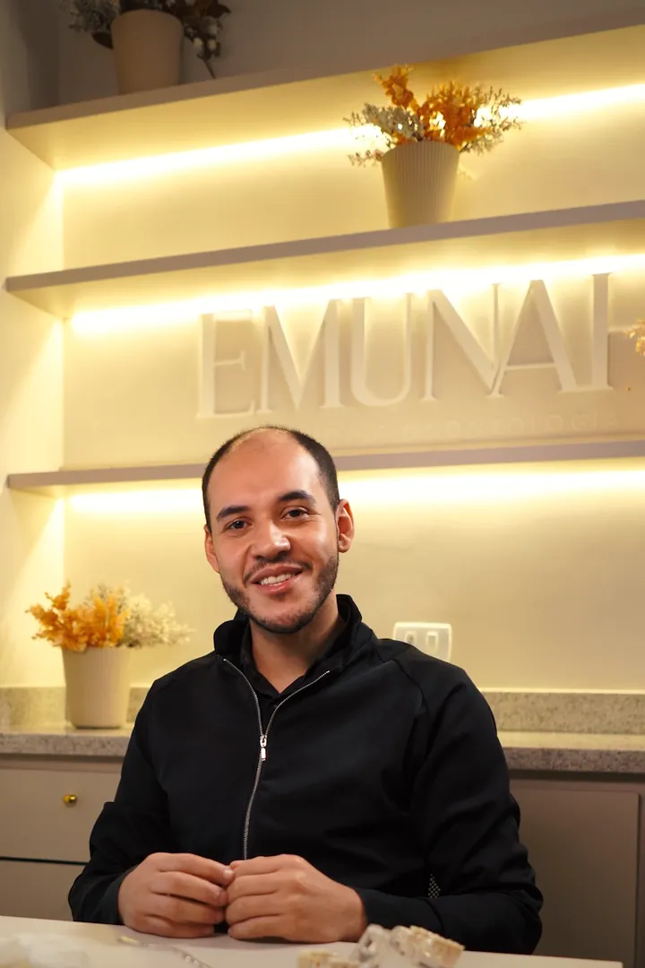 O dentista da Emunah diante da parede de luz com o letreiro EMUNAH